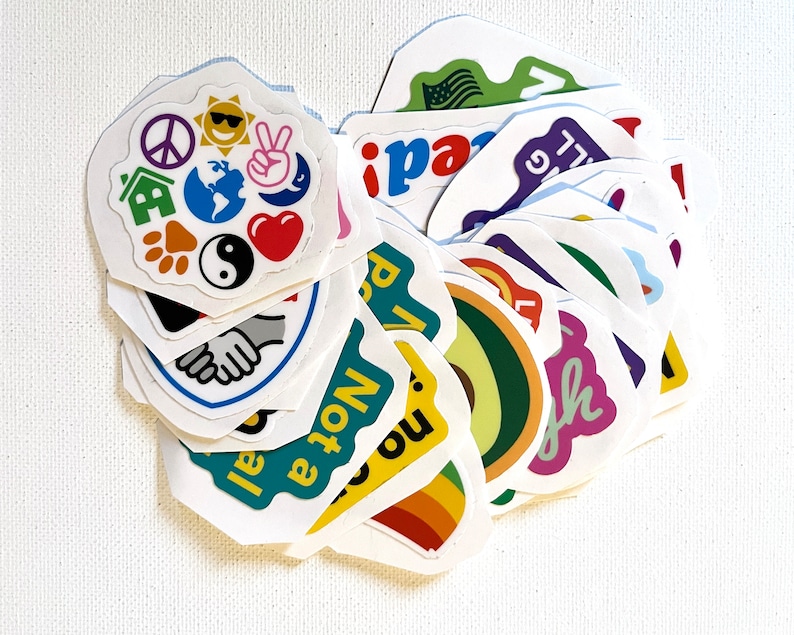 May include: A collection of colorful stickers with various designs and phrases, including peace signs, a globe, a house, a paw print, a yin yang symbol, a heart, a rainbow, an avocado, and the words "I am not a pro", "no", "peace", "laugh", and "I'll be back".