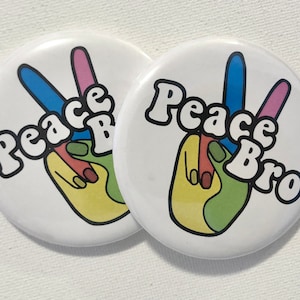 May include: Two white round buttons with a peace sign and the text "Peace Bro" in black. The peace sign is multi-colored with blue, pink, green, and yellow.