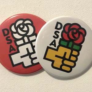 May include: Two round buttons with the letters DSA and a stylised image of a fist holding a rose. One button is red and the other is white.
