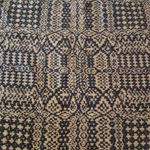 May include: A close-up of a fabric with a brown and black geometric pattern. The pattern is made up of small squares and diamonds.