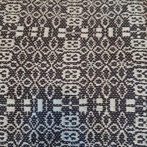 May include: A close-up of a woven fabric with a geometric pattern in black and white. The fabric has a textured surface and a repeating design.