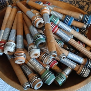 May include: A wooden bowl filled with a collection of vintage wooden spools with metal and colorful plastic accents. The spools are used for winding yarn or thread.