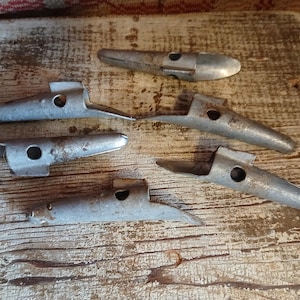 May include: Six vintage metal tools with a silver finish are arranged on a weathered wooden surface. Each tool has a unique shape, featuring a pointed end and a circular hole. The tools show signs of age and wear.