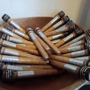 May include: A bowl filled with wooden spools wrapped in silver tape. The spools have black and blue accents at the ends.