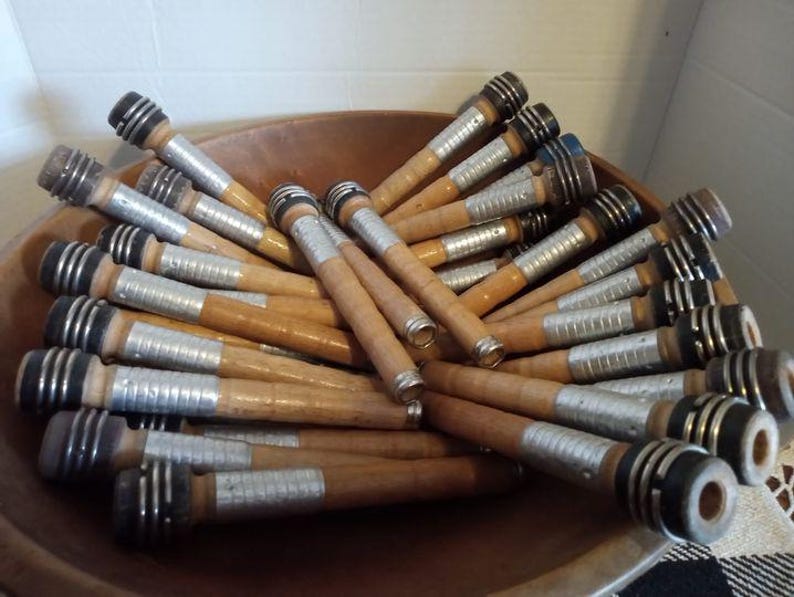 May include: A bowl filled with wooden spools wrapped in silver tape. The spools have black and blue accents at the ends.