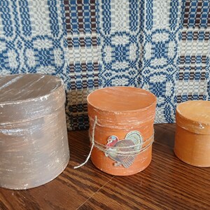 May include: Three antique, round, wooden boxes in varying sizes and colors. The largest is brown with white accents, the middle one is orange with a turkey sticker and twine, and the smallest is light orange.