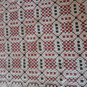 May include: Close-up of a woven textile with a repeating geometric pattern. The design features squares and rectangles in red, black, and off-white, creating a textured surface. The pattern is intricate and detailed, suitable for home decor.