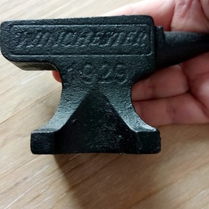May include: A black metal miniature anvil with the text "Tankefter" and "1926" engraved on the top.