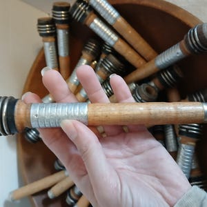 May include: A close-up of a wooden spool with a silver metal band. The spool is held in a hand. The spool is one of many in a bowl.