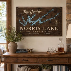 May include: A rectangular dark wood wall sign featuring a light blue map of Norris Lake, Tennessee. The text reads The Youngs, NORRIS LAKE, TENNESSEE, and LAKE HOUSE EST. 2017. A compass rose is positioned on the right side of the lake map.