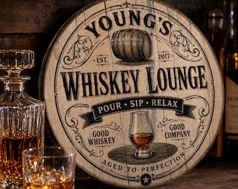 May include: Round wooden sign with the text "Young's Whiskey Lounge" and a whiskey barrel illustration. The sign includes the words "Pour, Sip, Relax" and "Good Whiskey, Good Company". A whiskey glass and decanter are visible.