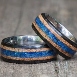 May include: Two wooden rings with blue and black inlay. The rings are stacked on top of each other.
