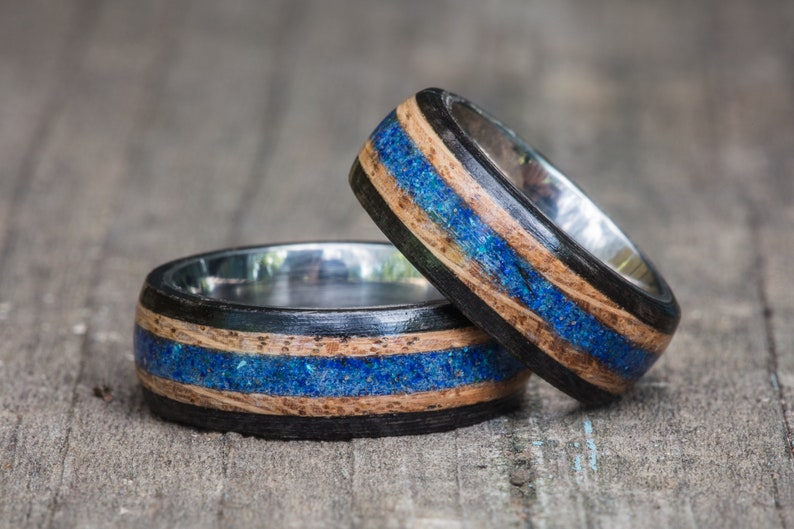 May include: Two wooden rings with blue and black inlay. The rings are stacked on top of each other.