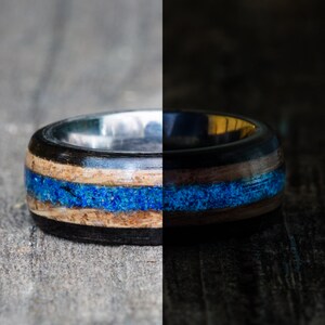 May include: A close-up of a wooden ring with a blue inlay. The ring is made of dark wood and has a silver band.