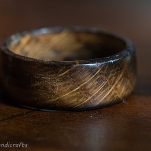 May include: A dark brown wooden ring with a smooth, polished finish. The ring has a unique grain pattern and is made from natural wood.