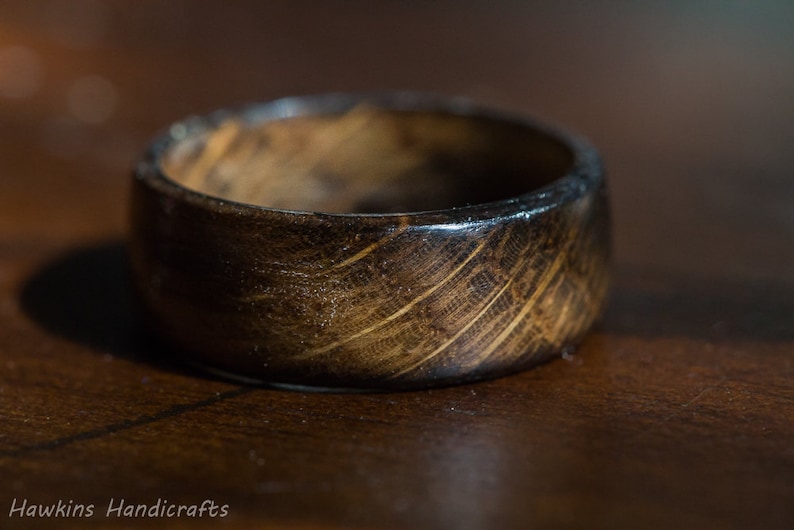 May include: A dark brown wooden ring with a smooth, polished finish. The ring has a unique grain pattern and is made from natural wood.