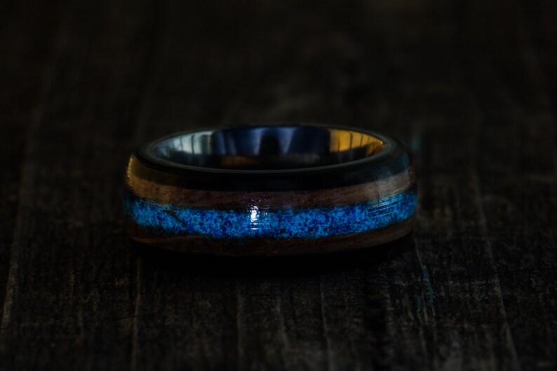 May include: A dark blue and brown wooden ring with a thin blue inlay. The ring is made of wood and has a polished finish.