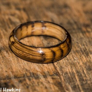 May include: A wooden ring with a dark brown and light brown striped pattern. The ring is made of wood and has a smooth, polished finish.