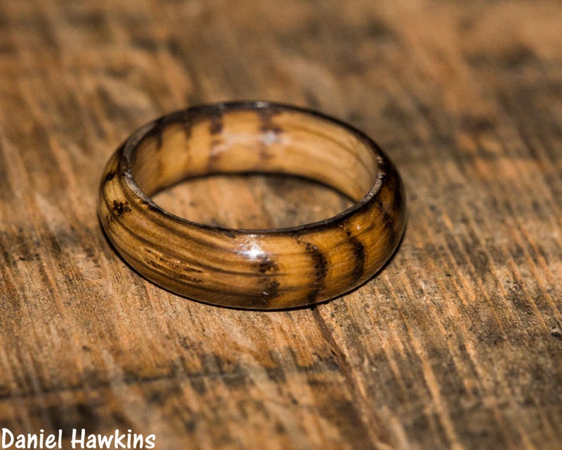 May include: A wooden ring with a dark brown and light brown striped pattern. The ring is made of wood and has a smooth, polished finish.