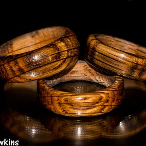 May include: Three wooden rings with a dark brown wood grain and a glossy finish. The rings are stacked on top of each other.
