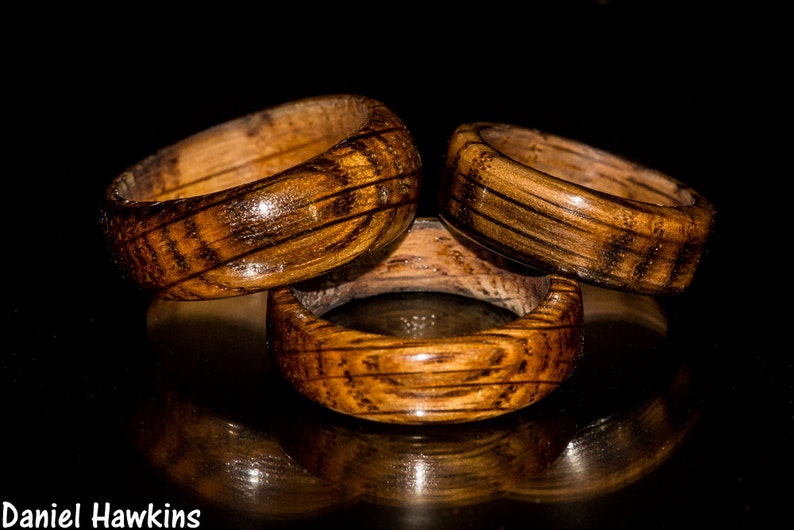 May include: Three wooden rings with a dark brown wood grain and a glossy finish. The rings are stacked on top of each other.
