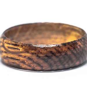 May include: A dark brown wooden ring with a natural wood grain pattern. The ring has a smooth, polished finish.