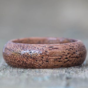 May include: A close-up of a wooden ring with a dark brown color and a natural wood grain pattern.