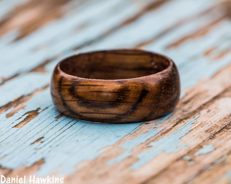 May include: A dark brown wooden ring with a smooth, polished finish. The ring has a wide band and a slightly rounded edge.