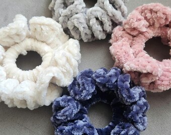 May include: Four scrunchies in different colors: white, gray, pink, and blue. The scrunchies are made of a soft, fuzzy material.