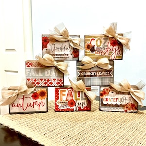 May include: A collection of six rectangular wooden blocks decorated with autumn-themed graphics, including pumpkins, sunflowers, and foliage. Each block features text such as Thankful, Cozy days, Fall days, Crunchy leaves, Autumn, Fall fun, and Grateful heart.