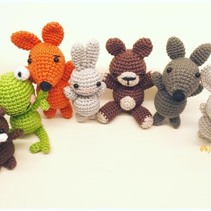 Puede incluir: Una colección de siete animales de peluche tejidos a crochet, incluyendo una rana, un zorro, un conejo, un oso, un ratón y otros dos animales. Los animales son todos de diferentes colores y tienen diferentes expresiones faciales.