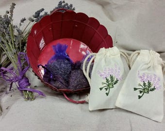 May include: Two small white fabric bags with lavender embroidery, filled with dried lavender flowers, and a red metal bowl filled with lavender sachets.