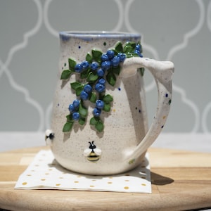 Handgemaakte keramische mok met bosbessen en bijen: blauw geglazuurd aardewerk