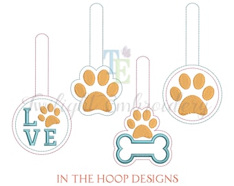 May include: Embroidered dog-themed designs in various shapes. Includes a paw print, a bone, and a circle with the word "LOVE" and a paw print. Each design has a hanging loop. The designs are in shades of orange, blue, and white.