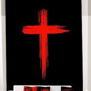 Könnte beinhalten: Roter Kreuz-Aufkleber an einer schwarz gestrichenen Wand. Der Aufkleber ist ein schlichtes Design im Pinselstrich-Stil. Die Wand befindet sich hinter einem weißen Sofa mit roten, schwarzen und weißen Kissen.