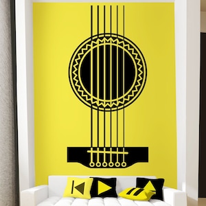 Könnte beinhalten: Ein schwarzer und gelber Gitarren-Silhouetten-Wandaufkleber an einer gelben Wand über einem weißen Sofa mit schwarzen und gelben Kissen. Der Aufkleber zeigt eine Gitarre mit einem Schallloch und Saiten.