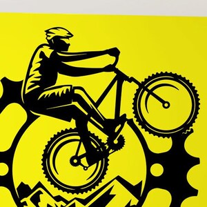 Könnte beinhalten: Schwarz-weißes Mountainbike-Aufkleber auf einer gelben Wand. Der Aufkleber zeigt einen Radfahrer, der mit einem Mountainbike über ein Gebirge fährt, mit einem Zahnrad im Hintergrund.