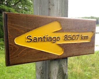 May include: A wooden sign with a yellow arrow pointing left. The arrow has the text "Santiago 8507 km" on it.