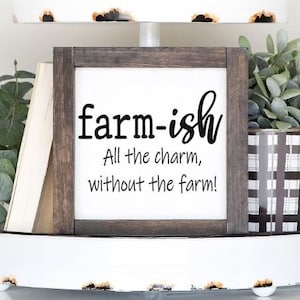 May include: A white tiered tray with a wooden sign that reads "farm-ish All the charm, without the farm!" The tray is decorated with greenery, a wooden book, and a white ceramic object with a beaded garland.