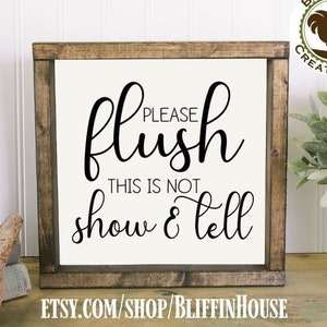 May include: A brown wooden sign with white text that reads "Please flush this is not show & tell". The sign is hanging on a white wall.