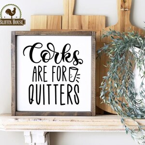 May include: A rustic wooden sign with the text "Corks are for quitters" in black lettering. The sign is displayed on a white shelf with a white pitcher and greenery.