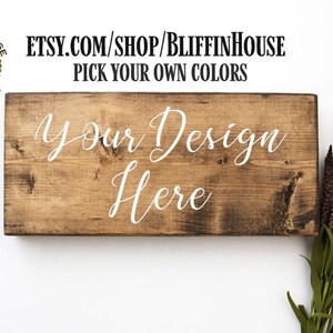 Puede incluir: Un letrero de madera con el texto "Your Design Here" en pintura blanca. El letrero est&aacute; hecho de madera natural con una mancha marr&oacute;n. El letrero es perfecto para agregar un toque personalizado a cualquier hogar u oficina.