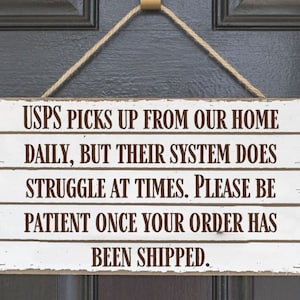 May include: White wooden sign with brown text that reads "USPS picks up from our home daily, but their system does struggle at times. Please be patient once your order has been shipped."