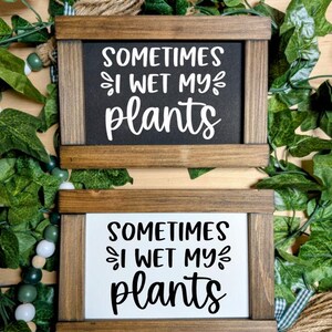 May include: Two wooden signs with the text "Sometimes I wet my plants" in black lettering on a white background and a black background. The signs are framed in brown wood.