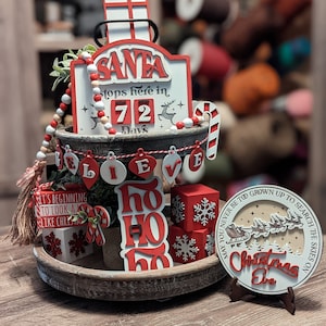 May include: A tiered tray decorated for Christmas with red and white wooden signs. The signs say "Santa Stops Here in 72 Days", "Believe", "Ho Ho Ho", and "May You Never Be Too Grown Up To Search The Skies On Christmas Eve".