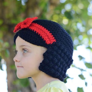 Puede incluir: Un gorro de ganchillo negro con un lazo y una diadema rojos. El gorro est&aacute; hecho a mano y presenta un punto texturizado. Este gorro es probablemente para un ni&ntilde;o y es un accesorio de disfraz.
