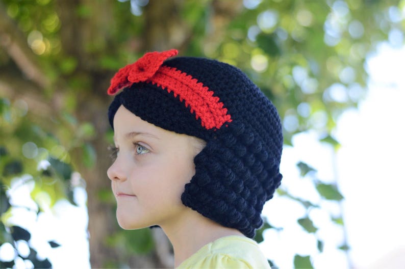 Puede incluir: Un gorro de ganchillo negro con un lazo y una diadema rojos. El gorro est&aacute; hecho a mano y presenta un punto texturizado. Este gorro es probablemente para un ni&ntilde;o y es un accesorio de disfraz.