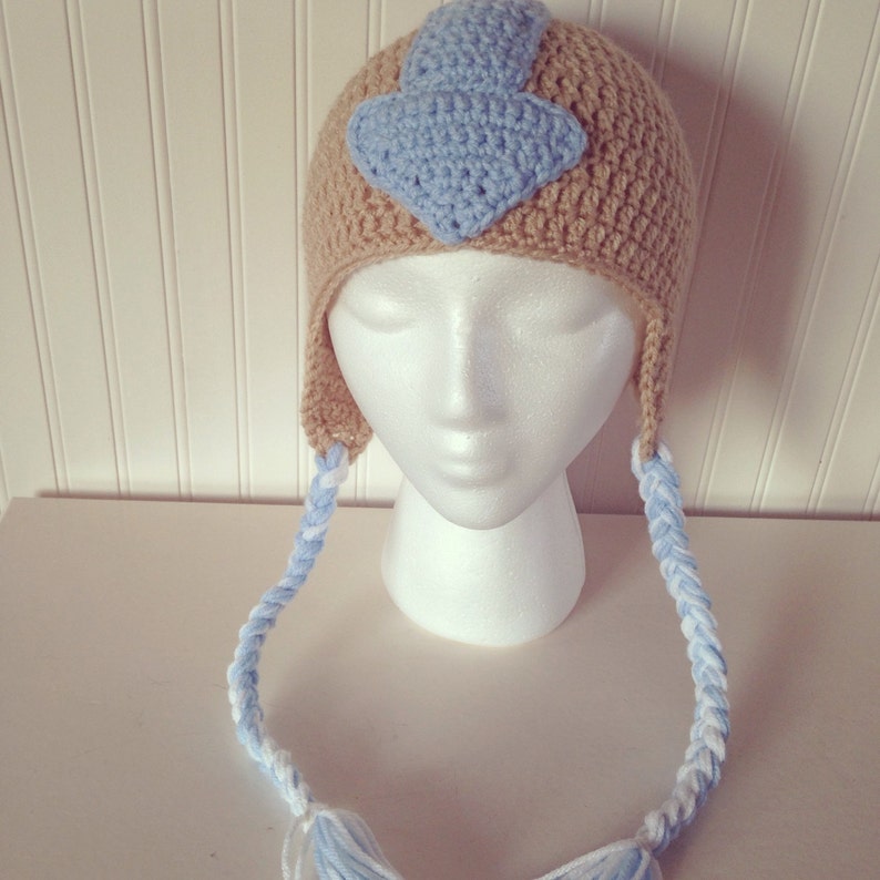 May include: A crocheted hat with a blue and white braid and a blue water tribe symbol on the front.