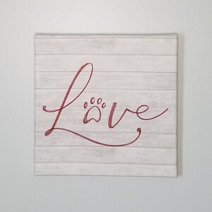 Word art wall sign any pet owner would "Love."  Embroidered in a script style has the word "LOVE" with a paw print in place of the "O."
