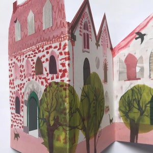 A concertina folded, shaped illustrated greetings card shpws a row of littel houses in pink, white and brown. Green trees line the street.